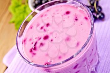 Milkshake with black currants in a glass on a purple napkin, saucer with berries currants on a wooden boards background
