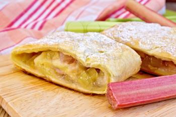 Strudel with rhubarb, napkin, rhubarb stalks on the background of wooden boards