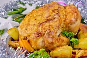 Chicken baked with vegetables and apples on a metal plate, silver toys, for branches on the background of wooden boards