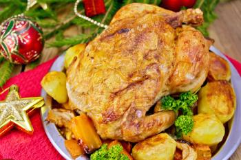 Chicken baked with vegetables and apples on a metal plate, red and gold Christmas toys, napkin, spruce twigs on a wooden boards background