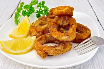 Crispy fried calamari rings on a plate with slices of lemon and parsley on a wooden boards background