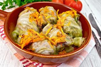 Stuffed cabbage meat in cabbage leaves with roasted carrots in a ceramic pan on a napkin, tomatoes, parsley on a lighter background board