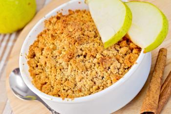 Crumble with pears in a white bowl on a wooden board, pear, cinnamon, spoon on a background of a linen tablecloth