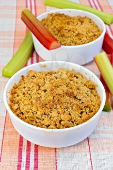 Rhubarb crumble in two white bowls, rhubarb stalks on linen tablecloth background