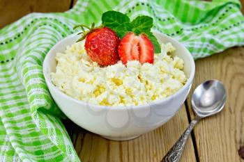 Cottage cheese in white bowl with strawberries and mint, spoon, napkin on the background of wooden boards