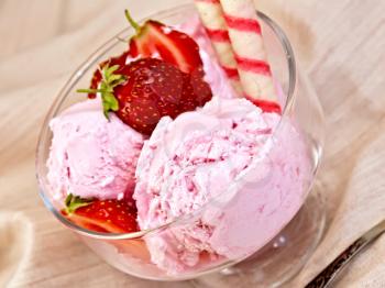 Strawberry ice cream in a glass bowl with wafer rolls and strawberries, spoon on a cloth background