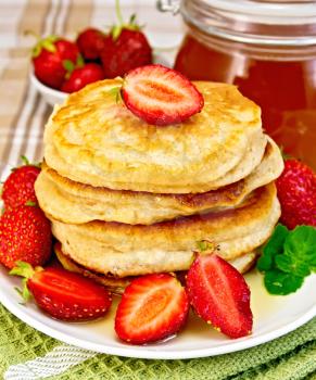 A stack of pancakes with strawberries and honey on a white plate, a jar of honey on the background of a linen tablecloth