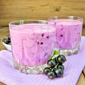 Milkshake with black currants in two low glass jars on a purple napkin, saucer with berries currants on a wooden board