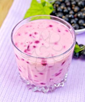 Milkshake with black currants in a glass on a purple napkin, saucer with berries currant and leaves on the background of wooden boards
