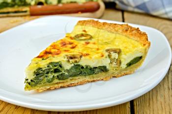 One piece of the pie with spinach, cheese and olives on a plate, knife, napkin on the background of wooden board