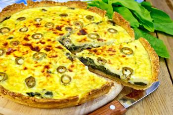 Pie with spinach, cheese and olives on a round board, spinach leaves, knife, napkin on the background of wooden boards
