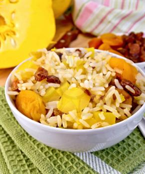 Fruit Pilaf with pumpkin, raisins, dried apricots in a bowl on a napkin, pumpkins, dried fruit, napkin, spoon on a wooden boards background