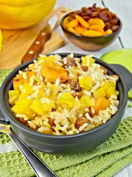 Fruit Pilaf with pumpkin, raisins, dried apricots in a black pan on a napkin, pumpkins, dried fruit, napkin, spoon on a wooden boards background