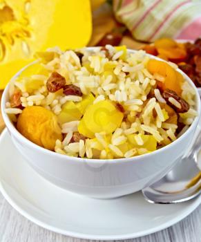Fruit Pilaf with pumpkin, raisins, dried apricots in a bowl, napkin, pumpkins, dried fruit, napkin, spoon on a wooden boards background