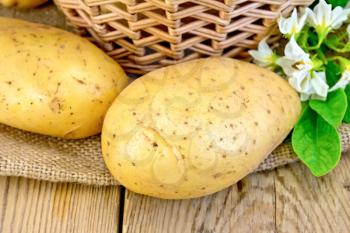 Yellow potato tubers with a flower on burlap, wicker basket on the background of wooden boards