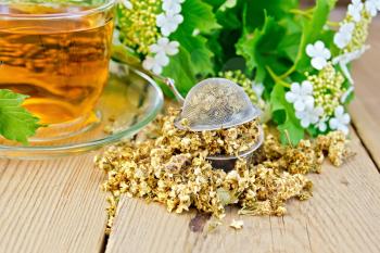 Metal sieve with dry flowers of viburnum, tea in a glass cup, fresh flowers of viburnum on a wooden boards background