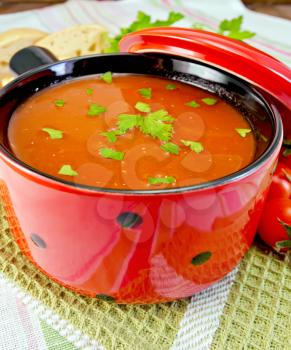 Tomato soup in a red ware on a green napkin, tomatoes, bread, parsley on a linen tablecloth background