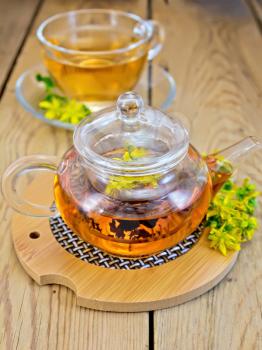 Tea in a glass teapot on stand, a cup of herbal tea, fresh flowers of Hypericum on a wooden boards background