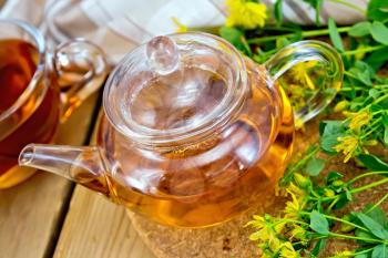 Tea in a glass teapot on stand, cup, napkin, fresh flowers tutsan on the background of wooden boards
