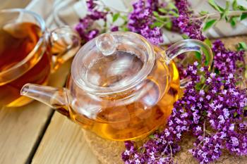 Herbal tea in a glass teapot and cup, fresh flowers oregano, napkin on a wooden boards background