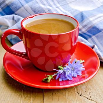 Chicory drink in a red cup with flower and napkin on a wooden boards background