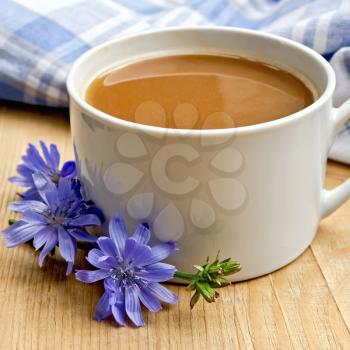 Chicory drink in a white cup with flower and napkin on a wooden boards background
