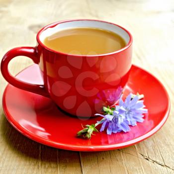 Chicory drink in a red cup with flower on a wooden boards background