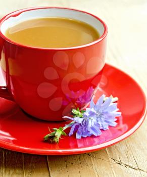 Chicory drink in a red cup with flower on a saucer on a wooden boards background
