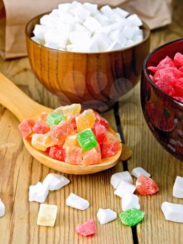 Candied papaya and coconut in bowls, colorful pieces of candied fruit in a spoon, a paper bag on a wooden boards background