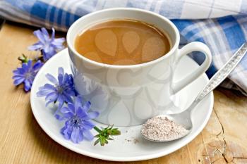 Chicory drink in a white cup with a flower and a spoon on the saucer, napkin on a wooden boards background