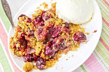 Cherry crumble in a white bowl with a spoon and ice cream on a background of striped linen napkin