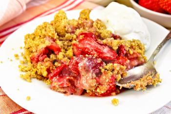 Strawberry crumble in plate with a spoon on a napkin, strawberries on a wooden boards background