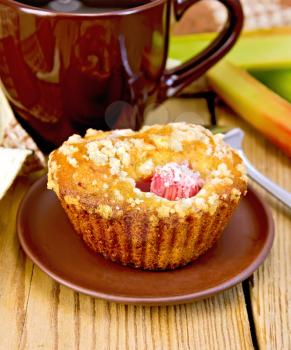 Cupcakes with rhubarb on a plate, cup, napkin, rhubarb stalks on a wooden boards background