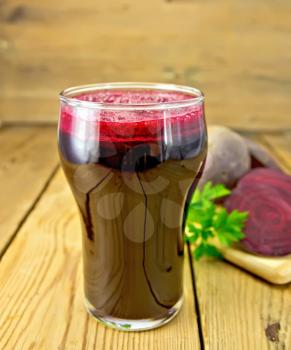 Beet juice in a high glass beaker, beets, parsley on a wooden boards background