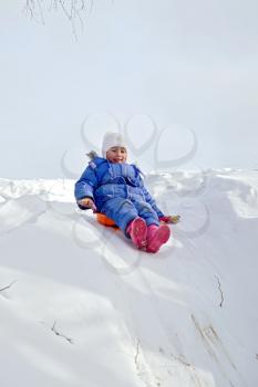 Little girl on a sled sliding down a hill on snow in winter