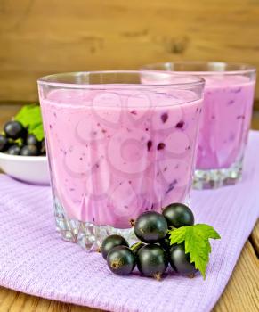 Milkshake with black currants in two low glass jars on a purple napkin, saucer with berries currants on a wooden boards background