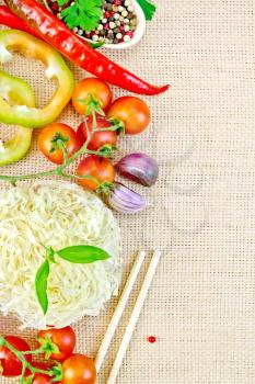 Rice noodles curled, tomatoes, different peppers, basil, garlic, parsley, sticks on the background of sack cloth