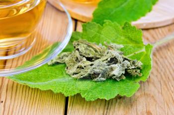 Dried sage on fresh leaves of sage tea in a glass cup on a wooden boards background