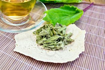 Dried sage on paper, fresh sage leaves, tea in a glass cup on a background of bamboo napkins and wooden planks