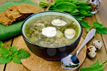 Green soup of sorrel, nettles and spinach in a bowl of quail eggs, bread, pepper, spoon on a wooden boards background
