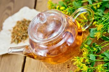 Tea in a glass teapot on stand, fresh and dried flowers of Hypericum on a wooden boards background