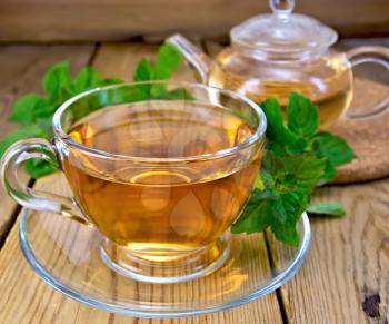 Herbal tea in a glass cup and teapot, fresh leaves of mint on a wooden boards background