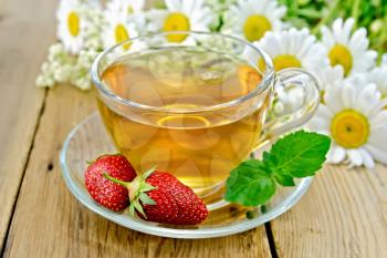 Tea with strawberries in a glass cup, a bouquet of daisies on a background of wooden boards
