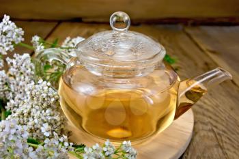 Yarrow tea in a glass teapot, fresh yarrow flowers on a wooden boards background