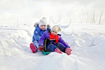 Two little girls on a sled in the snow in the winter