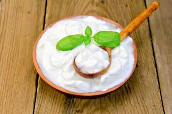 Thick yogurt in a clay bowl with basil and spoon on a wooden boards background