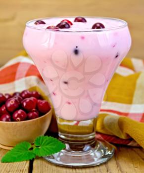 Thick yogurt in a glass goblet with cranberries, spoon, napkin, cranberries in a bowl, mint on a wooden board