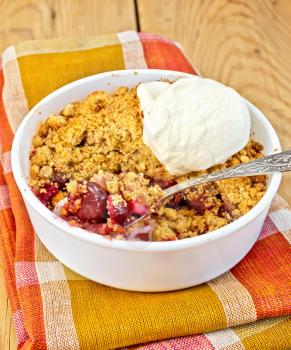 Cherry crumble in a white bowl with a spoon and ice cream on a napkin on a wooden boards background