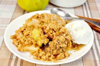 Crumble with pears and ice cream in a white plate, spoon, pear, cinnamon on a background of a linen tablecloth