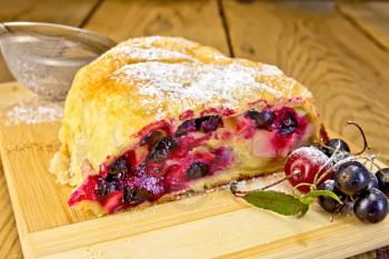 Strudel with black currants and berries, strainer on a wooden boards background